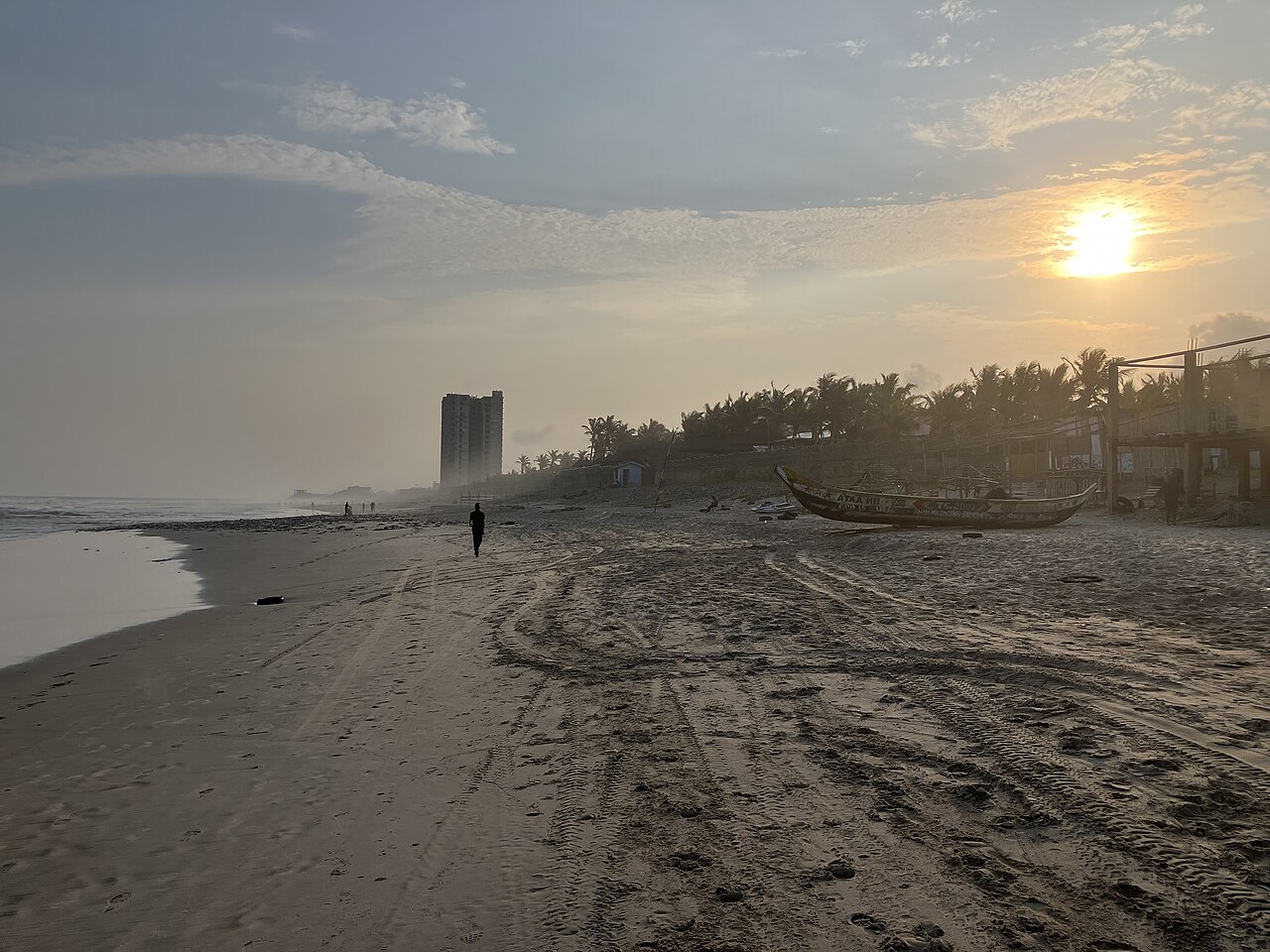 Evening light over Labadi Beach in Accra, with a fishing boat and a lone walker on the sand